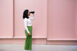 © VISTA by Westend61 - Woman in casuals looking through binoculars and standing in front of pink wall