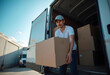 © PTD - young man is carrying cardboard box from delivery truck, showcasing busy logistics environment. scene reflects hard work and dedication in transportation industry