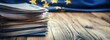© Vergiliy - Documents stacked beside European Union flag, wooden table background