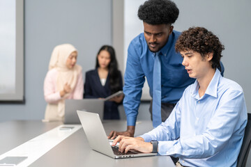 Diverse team of business professionals working on laptops during corporate meeting analyzing data and discussing project strategies, focused on collaboration, productivity and effective communication