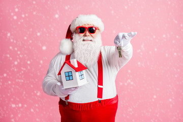 Portrait of his he nice attractive cheerful Santa holding in hands house giving you keys property insurance offer deal comfort rental service isolated over pink pastel color background