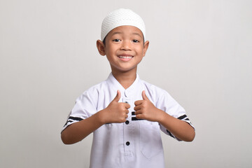 Portrait of a Muslim Asian boy smiling happily and giving a thumbs up isolated on a white background.