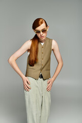 With his striking red hair, a teenager elegantly poses in a stylish smart casual ensemble against grey.