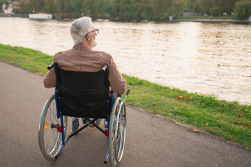 Wall Mural - Sad senior man sitting in wheelchair walking on road in city park outdoor, back view. Old paralyzed man in chair for people with disability feel depressed. Lonely elderly sick man sits on wheelchair