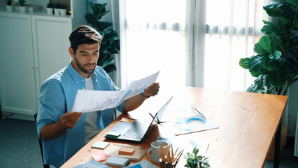 Skilled businessman writing idea on colorful sticky notes while looking at data analysis. Caucasian project manager working on laptop while taking a note in sticky notes at meeting room. Convocation.