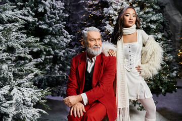 Wall Mural - A charming duo poses in winter attire amid frosted Christmas trees, capturing holiday spirit.