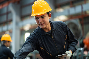 A man wearing a yellow hard hat and a black jacket is holding a tablet. He is focused on the tablet, possibly working on a project or reading instructions. Concept of professionalism and concentration