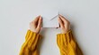 © Elkhan Babayev - Female hands in yellow sweater hold an open craft paper envelope and a white card with blank space, taken from a high, first-person perspective on a white background.