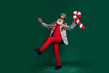 Full size photo of extravagant grandfather dance cane candy stick red trousers xmas tree toys blazer isolated on dark green color background