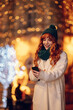 © Zamrznuti tonovi - A happy ginger woman is sending text messages on a street on new year's eve.