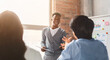 © Prostock-studio - Cheerful black employee talking to colleagues while business presentation, office interior