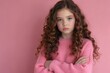 © MdAlamin - A young girl with long, curly brown hair is wearing a pink sweater and is standing with her arms crossed in front of a pink background