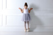 © New Africa - Little ballerina practicing dance moves near white wall indoors
