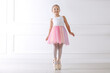 © New Africa - Little ballerina practicing dance moves near white wall indoors