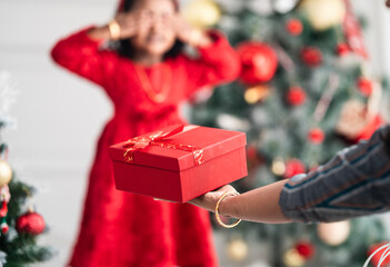 little girl closes her eyes and waits for a Christmas present, woman holding Surprise Christmas gift 