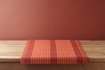 Canvas Print - Empty wooden table with bamboo tablecloth over brown wall background.  Kitchen mock up for design and product display