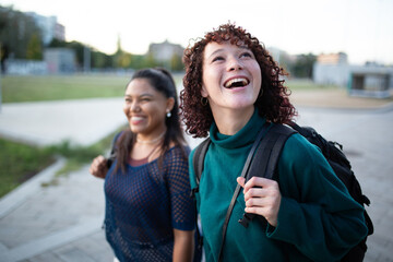 Two women walking and smiling outdoors with a city backdrop