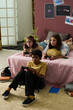 © pressmaster - Three children playing video games together on a sofa with controllers in hand, having focused expressions. Background shows books, plants, and educational posters