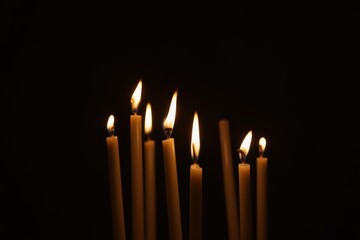 Multiple tall candles burning in a dark setting, casting warm light and shadows. Concept of meditation, spirituality, and ceremonial tradition