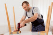 © Prostock-studio - Carpentry Service. Repairman In Blue Uniform Fixing Table With Electric Drill Standing Indoors. Furniture Assembler Man Assembling Wooden Desk Working In Studio