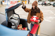 © Home-stock - Preparation for winter holidays. Excited woman packing Xmas wrapped gift boxes into car trunk, standing at parking lot of shopping mall