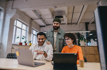 Wall Mural - Happy colleagues working together in office using laptops at office with coworkers