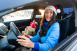 © Home-stock - Happy woman in Santa hat driving car after shopping Xmas presents, sitting in car with wrapped gift boxes nearby. Lady preparing for New Year and Merry Christmas