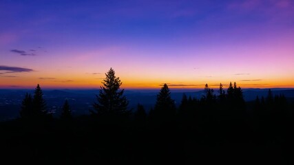 Wall Mural - Vivid twilight colors transform over a forest, creating a surreal and dreamlike atmosphere filled with vibrant hues of orange, purple, and blue against a tranquil backdrop of trees