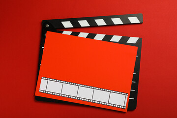 Clapperboard and red paper with film on red background, top view