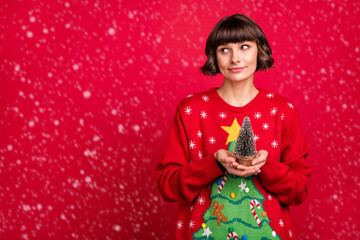 Portrait of attractive pensive girl holding in hands tiny tree thinking copy space isolated over red color background