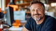 © Lens Legacy - A cheerful man in a dark shirt, surrounded by office elements, smiles with warmth and enthusiasm in a well-organized, energetic work environment.