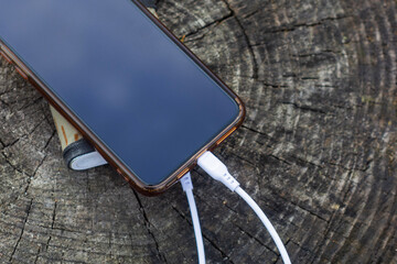 A portable charger charges the smartphone. Power Bank with cable against the background of wood