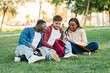 © Jose Calsina - Three young students studying and doing homework on a university campus lawn, engaged in learning, enjoying group study outdoors, diverse teenage friends sharing knowledge, preparing for exams