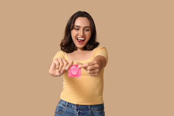 Happy young woman with condom on beige background. Safe sex concept