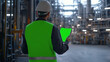 © RealityForge - Man in hard hat and reflective vest viewed from behind as he looks at a clipboard in an oil refinery. The clipboard is a chroma key green screen blank.