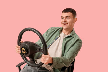 Happy young man with steering wheel on pink background