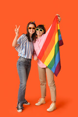 Wall Mural - Young lesbian couple with LGBT flag showing victory gesture on orange background