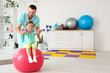 © Pixel-Shot - Male physiotherapist and little girl with dumbbells training on fitball in rehabilitation center
