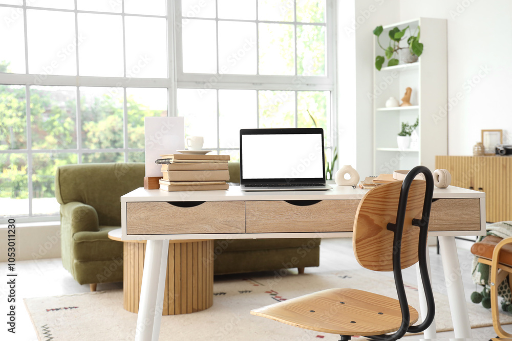 Blank laptop with books on programmer's desk in light living room