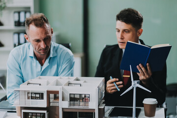 Engineers meeting about wind turbine model and house model. Renewable energy and housing development concept. Team of architects and engineers in modern office discussing design structure.