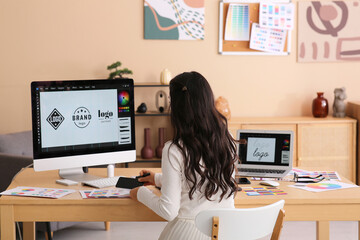 Wall Mural - Young female graphic designer working with computer and color palettes at table in office