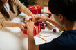 © snowing12 - A young man and woman are sitting at a table, joyfully passing a gift to each other in a festive, holiday setting. A decorated Christmas tree in the background.