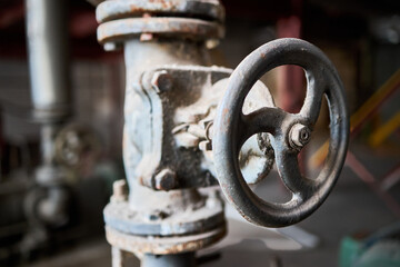 Industrial dusty chemical petrochemical retro style valve closeup with selective focus on steering wheel mounted with flange connection on pipe, out of focus foreground with copyspace.