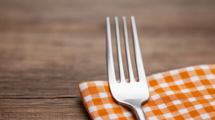 Rustic Elegance: A close-up of a gleaming fork resting on an orange gingham napkin, set against a warm wooden table.  Perfect for food blogs, restaurants, and culinary themes. 