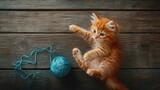 Fototapeta Koty - Playful Orange Kitten with Yarn Ball on Wooden Surface