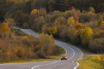 A red car drives on a lonely road in an autumn landscape