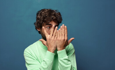 Wall Mural - covering face with hands, peeking between fingers with surprised expression and looking to the side