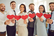 © Studio Romantic - Group of business people stands in the office, holding red hearts. Love and togetherness, possibly in a volunteer or valentine day context, showcasing a diverse team united in purpose.