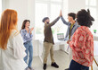 © Studio Romantic - Diverse group of happy young people in casual wear celebrating successful collaboration and teamwork. Multiracial team of colleagues standing in circle with two men giving high five to each other.