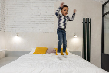 Kid jumping on the bed and looking enjoyed and contented